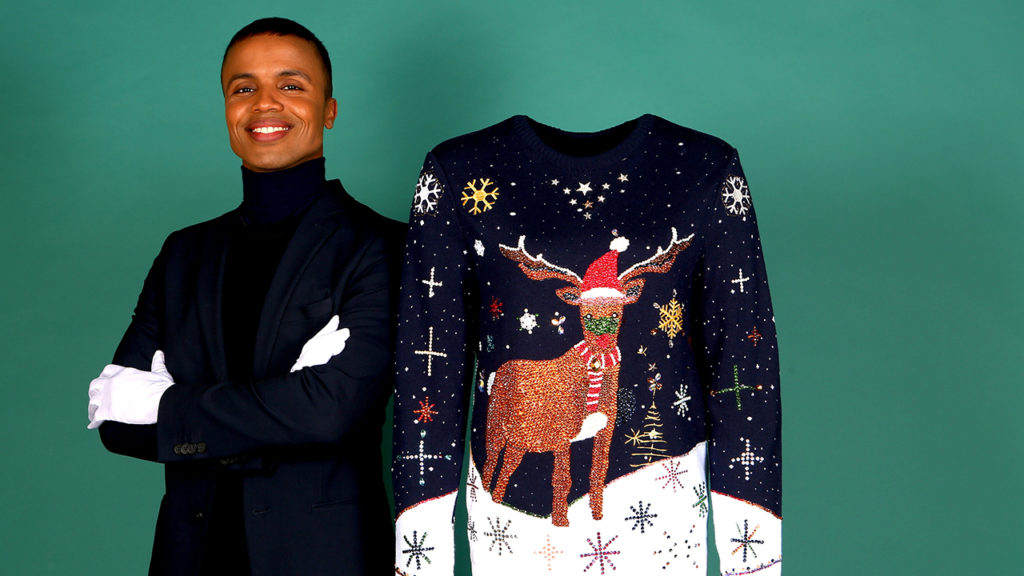 Man posing next to an expensive Christmas sweater featuring a reindeer in the snow. 