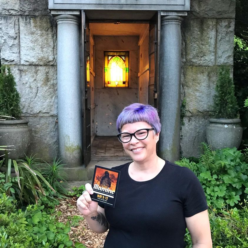 Author standing in front of a lit mausoleum in a cemetery for an event. 