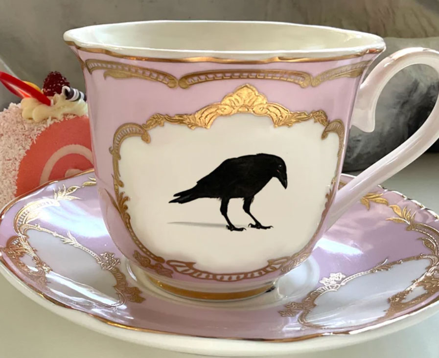 Pink, gold, and white tea cup set featuring a raven print. 