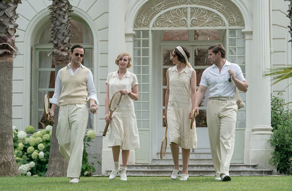 Two couples walking across a lawn on their way to a tennis game. 