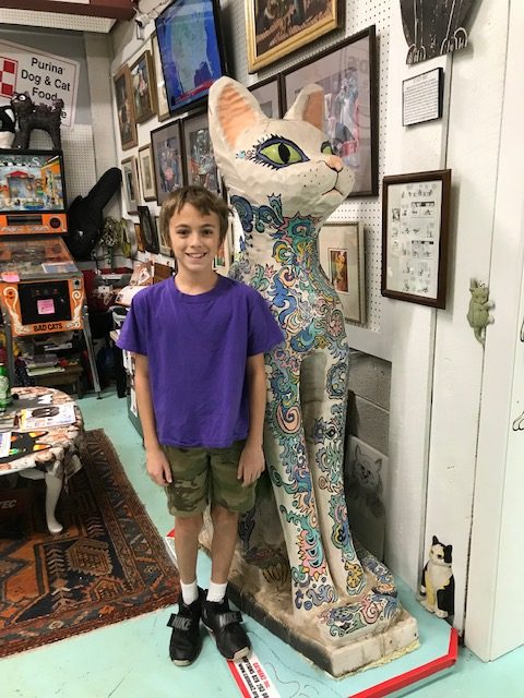 A young boy stands next to a large cat statute. 