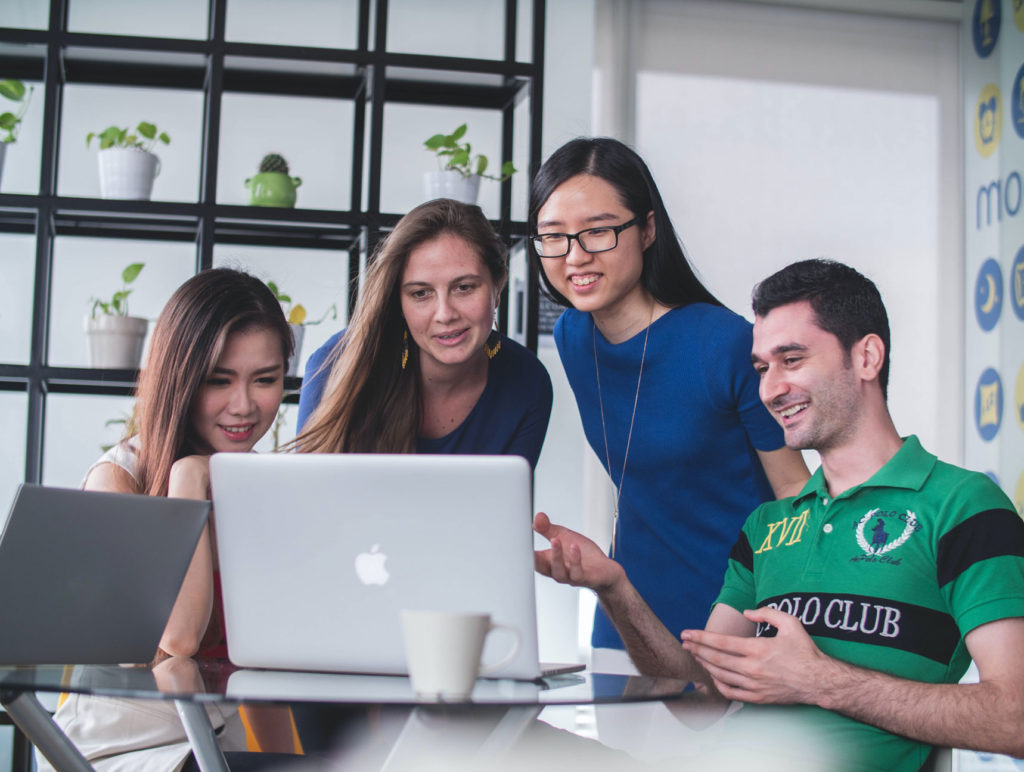 Four friends or co-workers gathered around a laptop.